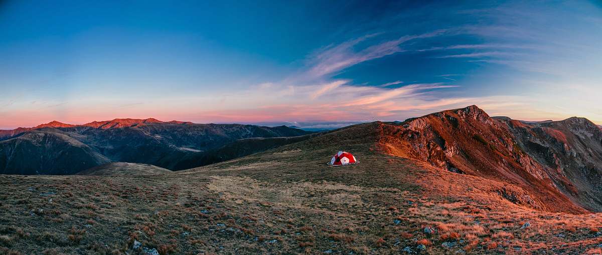 mountain range red and white camping tent on top of the mountain during daytime tent